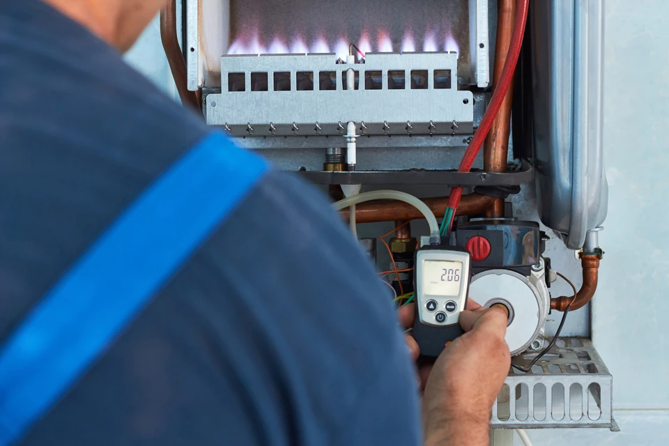 Technicien en bleu travaillant sur chaudière à gaz domestique, manipulation d'un multimètre digital affichant 206