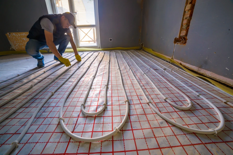 Ouvrier installant un système de chauffage au sol dans une pièce en rénovation