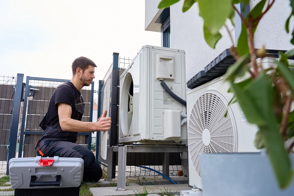 Technicien HVAC en uniforme vert travaillant sur système de chauffage/climatisation dans intérieur résidentiel