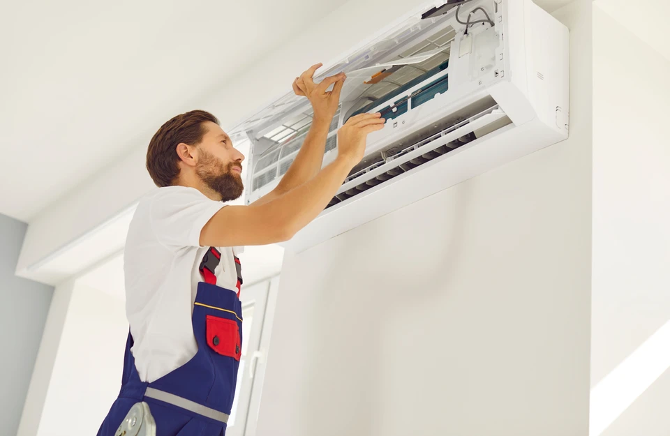 Technicien en combinaison bleue effectuant maintenance sur système de climatisation extérieur, utilisant manomètres de réfrigération