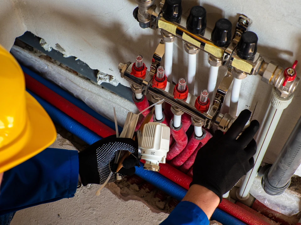 Plombier professionnel en casque de sécurité blanc travaillant sur installation de chauffage ou sanitaire dans local technique